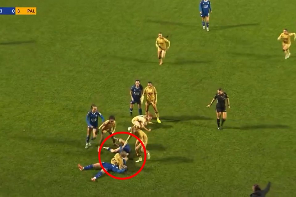 A women's soccer player in a blue uniform lies on the green field, with another player in a yellow uniform falling over her.