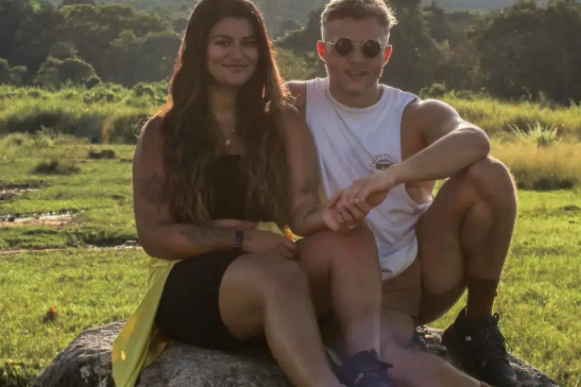 An image collage containing 1 images, Image 1 shows Two people sitting on a rock in a field with text "Cost of Living in Thailand per month"