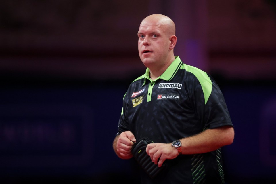 A bald man in a green and black polo shirt holding a darts case.