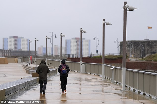 People walk along the seafront in the rain near Old Portsmouth in Hampshire this morning