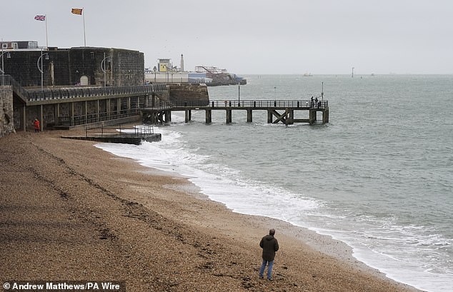 People walk along Hot Walls beach in Portsmouth this morning as the UK is hit by heavy rain