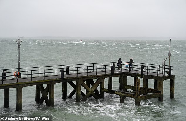 People walk along Victoria Pier in Portsmouth this morning as the UK is hit by heavy rain