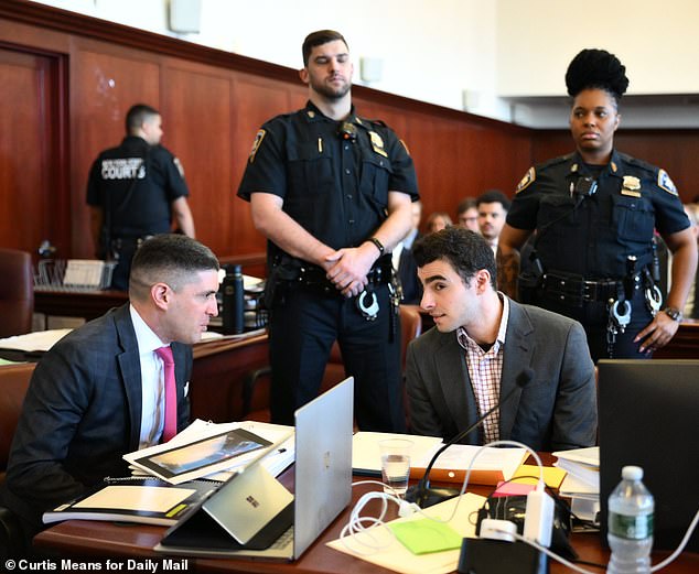 Mangione seen speaking with his attorney as two NYPD officers guard him inside Manhattan Supreme Court on Monday
