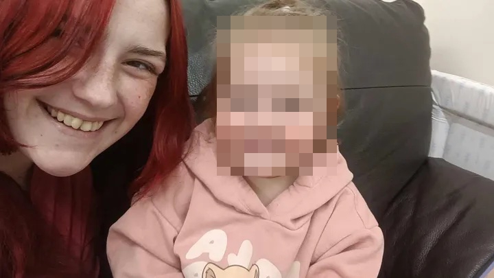 A woman with red hair smiling with a child next to her whose face is pixelated.