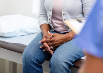 A woman clasps her hands during a discussion with medical personnel.