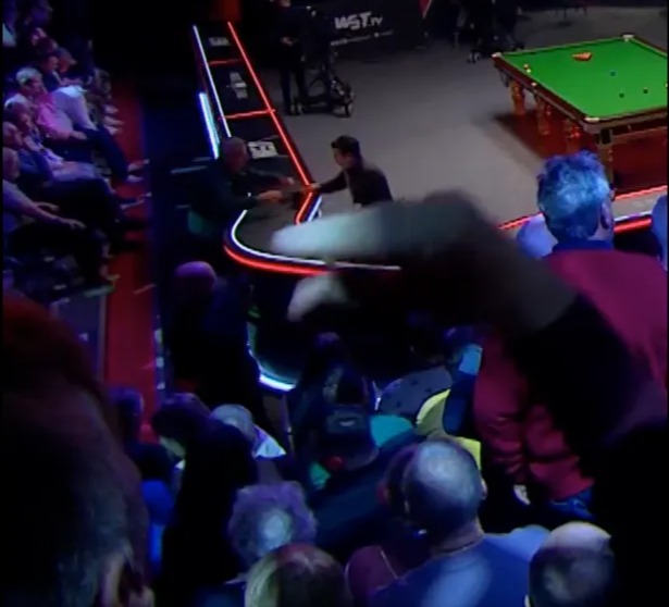 A snooker table with players and a crowd in a darkly lit room with colorful stage lights.