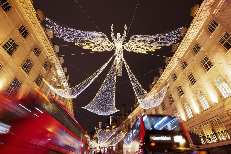 Regent Street, London, illuminated at night with Christmas lights shaped as angels and two red double-decker buses in motion blur.