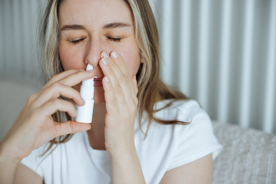 Woman in a white shirt with closed eyes using a nasal spray.