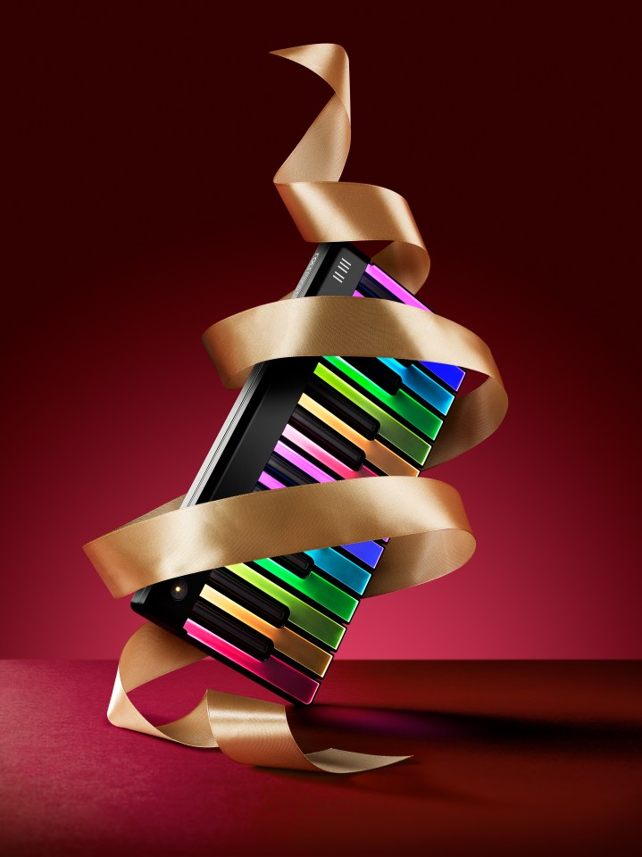 A black digital piano with colorful keys and a gold ribbon around it, on a red background.