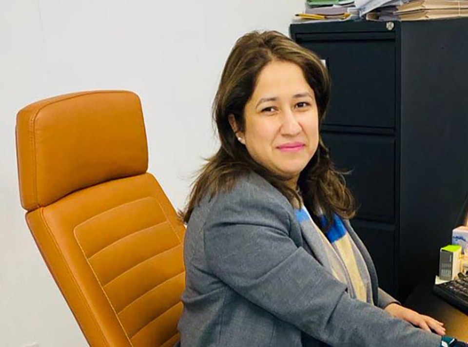 Woman with dark hair, wearing a gray blazer and striped scarf, sitting in an orange office chair.