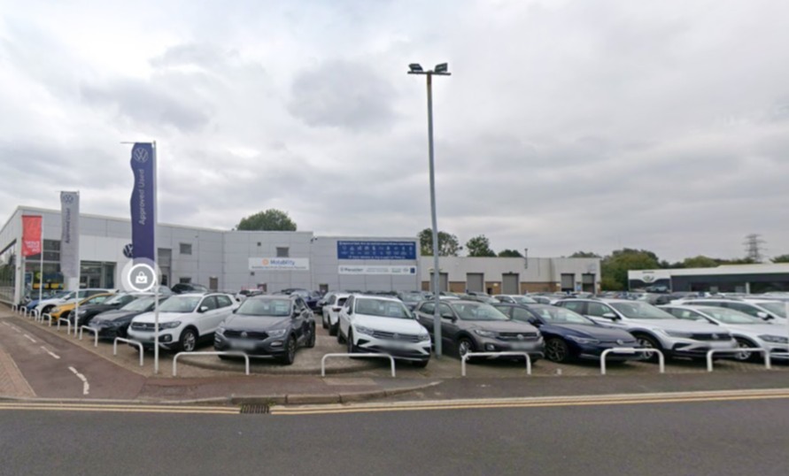 Car dealership with rows of cars parked in front of a white building with a Volkswagen banner.