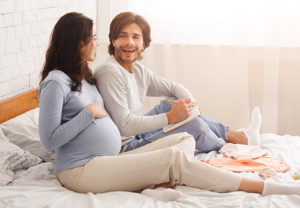 Pregnant couple choosing name for future baby, writing ideas to notebook