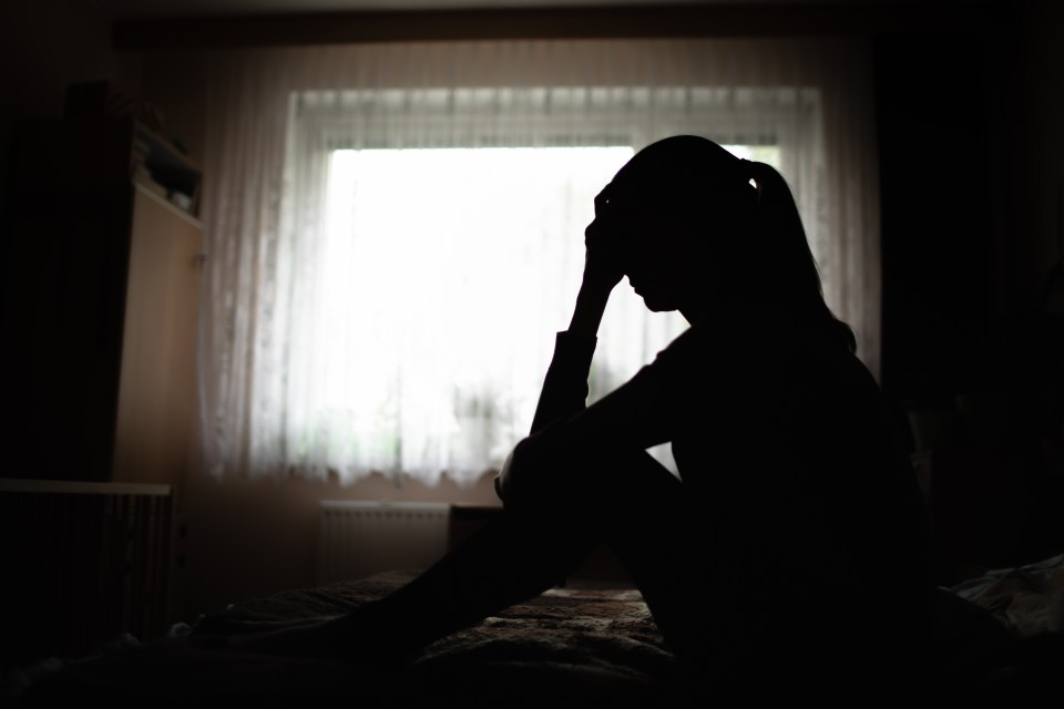 Silhouette of a woman sitting on her bed, head in hands, looking sleepless and anxious in a darkened room.