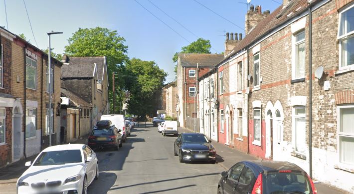 Street view of a residential road lined with cars and brick houses.