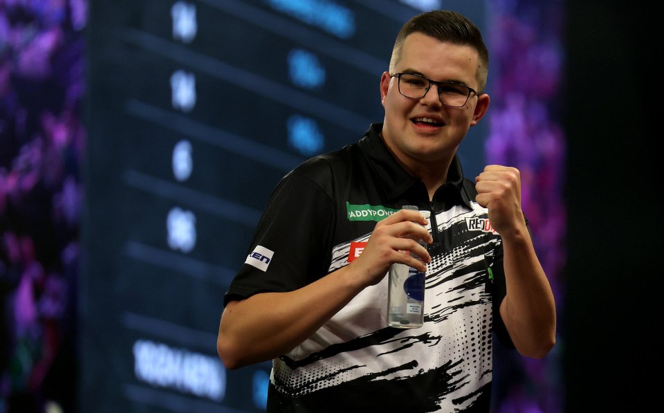 A male darts player in glasses holding a bottle and clenching his fist.