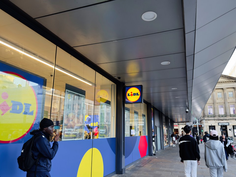 Customers walk past a Lidl store with bright blue and yellow branding in a modern shopping district.