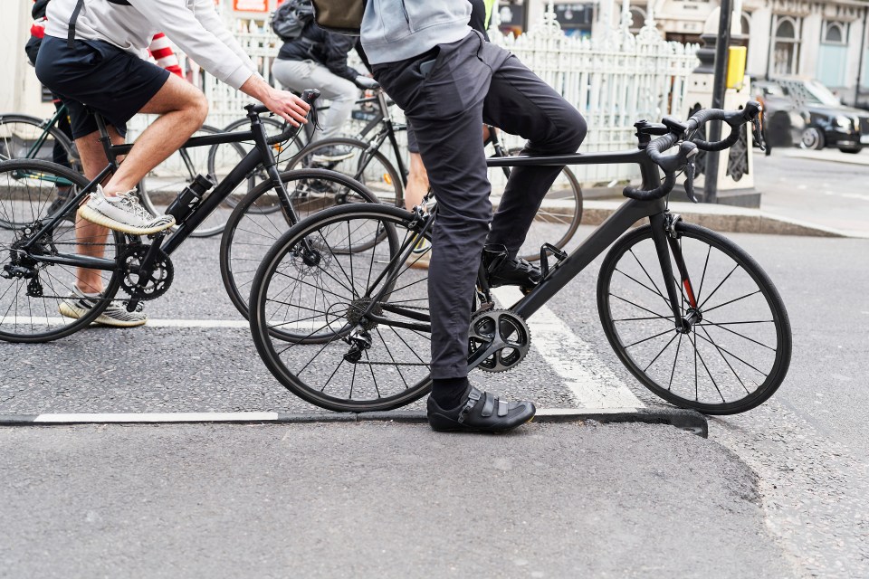 Side view of the legs of a group of people sitting on bicycles on the streets of London.