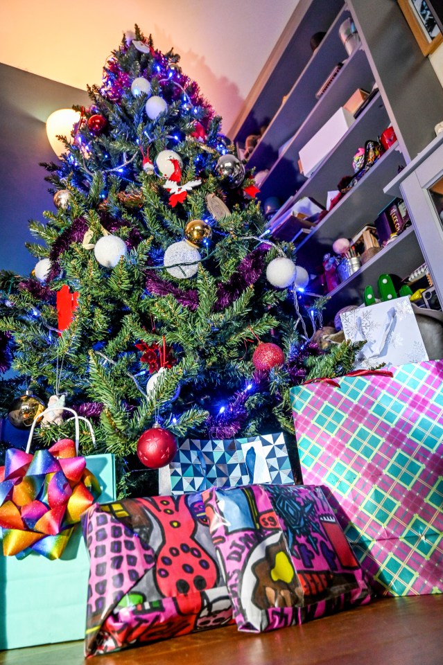 Christmas tree decorated with ornaments and blue lights, with wrapped gifts at its base.