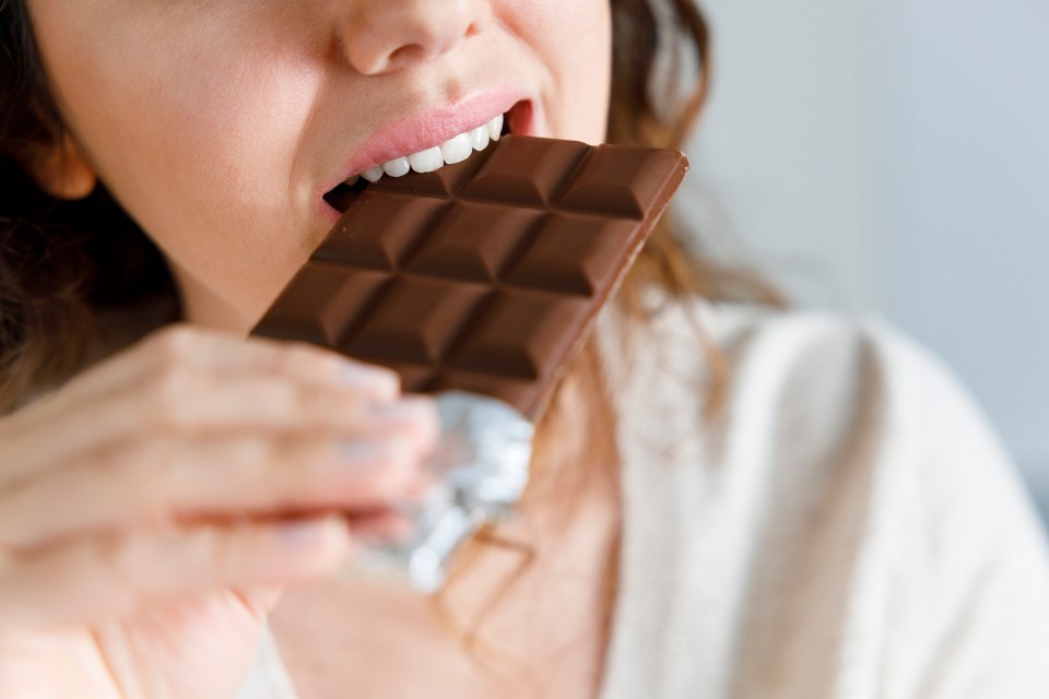 Young woman biting into a chocolate bar.