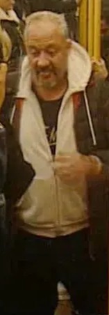 A man with a white beard and gray hair wearing a white jacket over a black shirt.