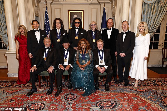 Jeanette Dousdebes Rubio, Secretary of State Marco Rubio, Paul Stanley, Gene Simmons, Peter Criss, Amb. Richard Grenell, Kennedy Center President, Amb. Sergio Gor, Amb. Monica Crowley and (Front Row L-R) Sylvester Stallone, George Strait, Gloria Gaynor, Michael Crawford pose for the class photo at the 48th Kennedy Center Honors Medallion Reception at the U.S. Department of State on December 06, 2025 in Washington, DC