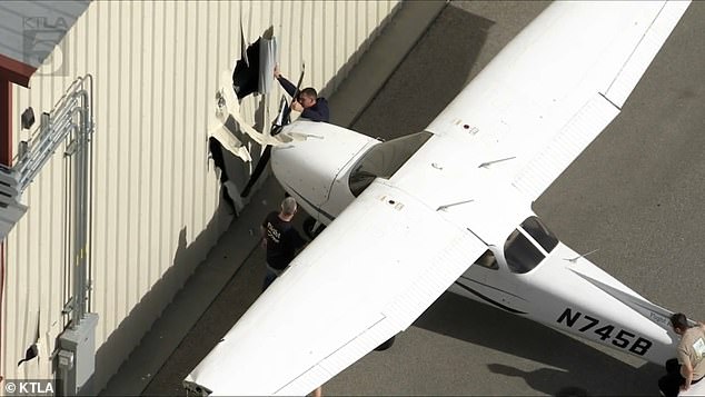 The plane has since been removed from the hangar and taken inside the flight school. Pictured are workers removing it from the hangar's exterior wall