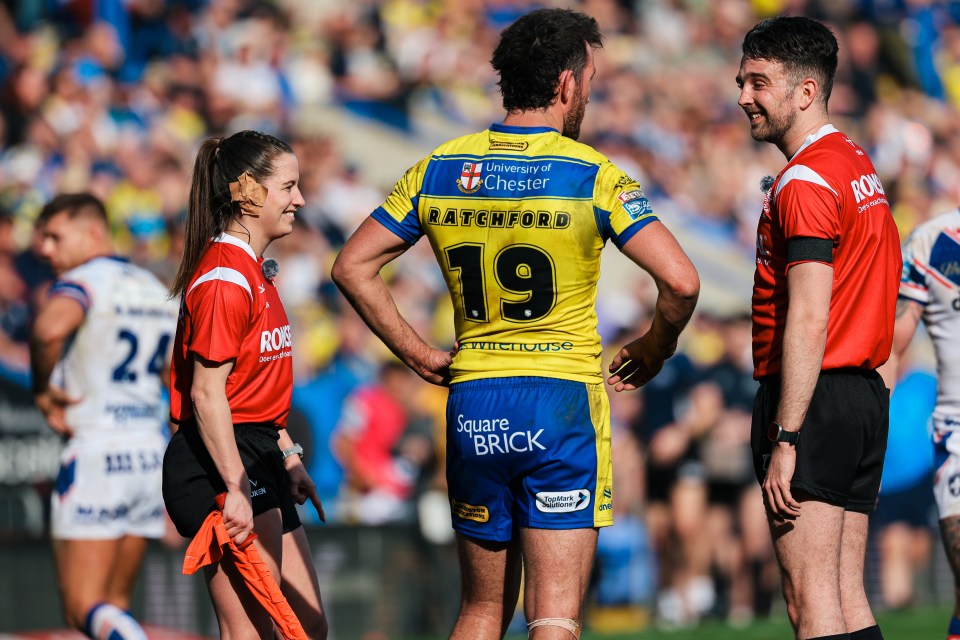 Tara Jones, the Super League touch judge, on a rugby field with two male players, smiling.