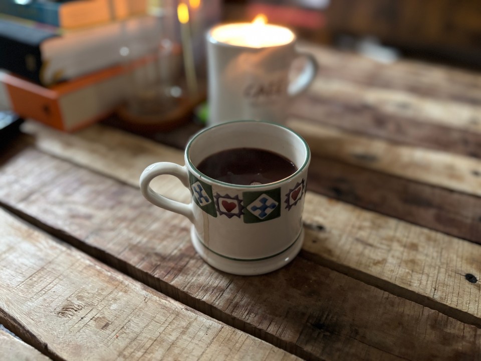 A mug with patterned hearts and crosses and a mug with a candle on a wooden table.