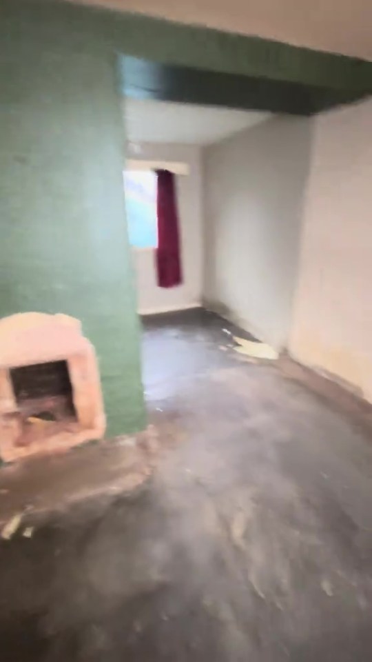 An empty, unkempt room with peeling paint and a bare floor, featuring an old fireplace.