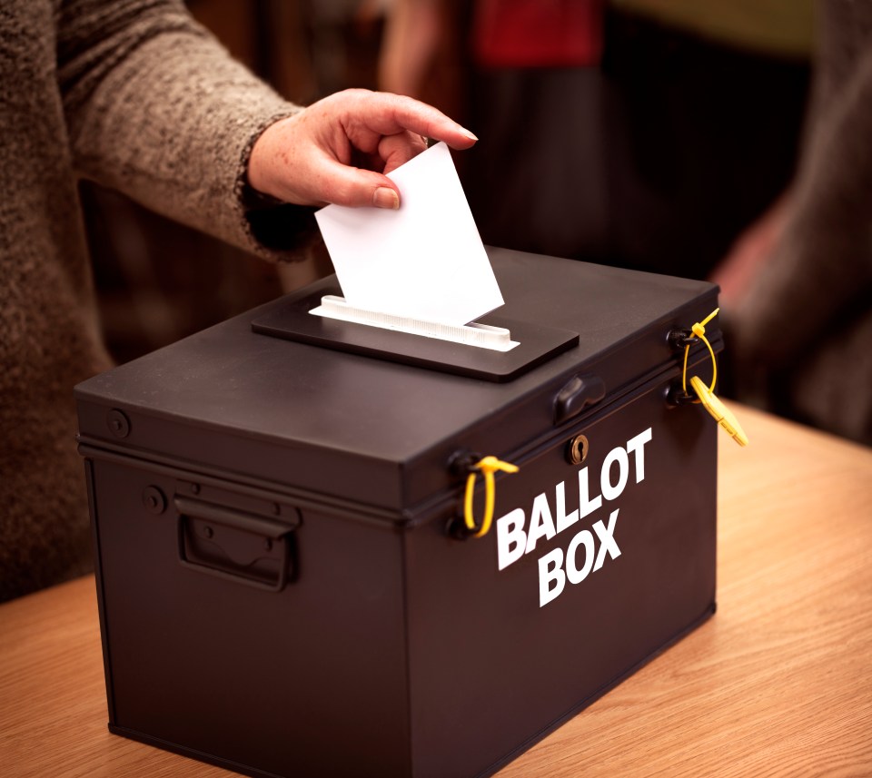 Person placing a vote into a black ballot box.