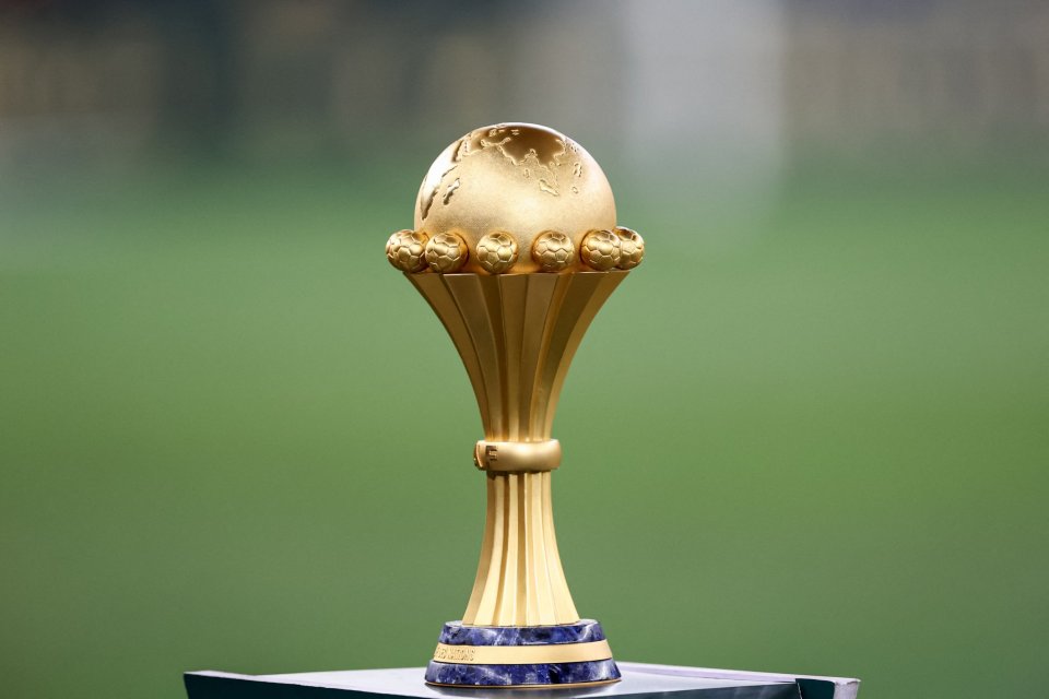 The golden Africa Cup of Nations trophy on a blue and gold base with a green background.