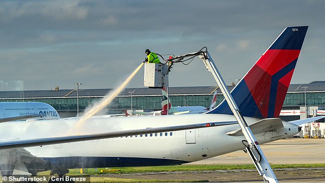 An airport worker is pictured spraying de-icing fluid onto an aircraft on a freezing winter morning in London