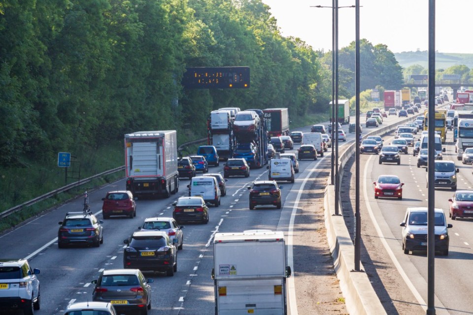 Vehicles in heavy traffic on a multi-lane highway next to a tree-covered hillside.
