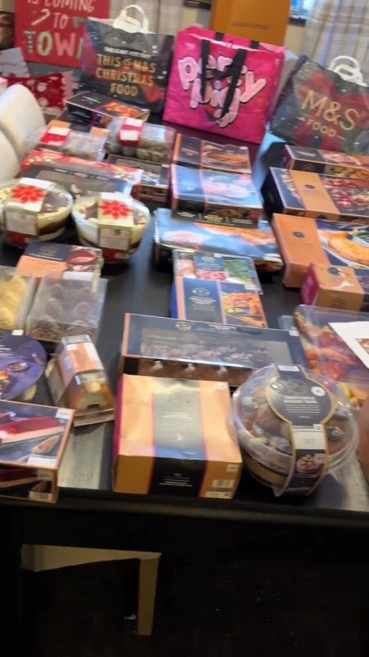 A table laden with Christmas food in boxes and bags, including trifles and pastries.