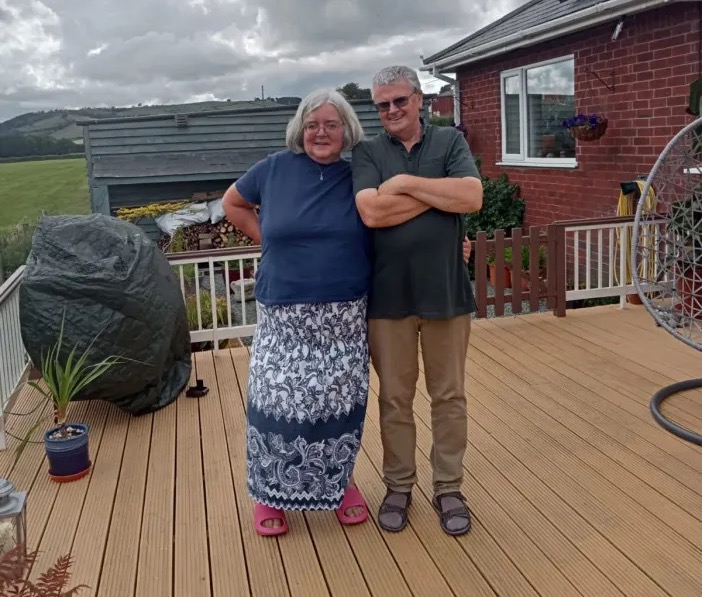 An elderly couple standing on a deck.