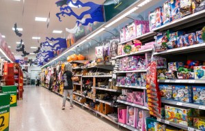 A child in a supermarket aisle decorated for Halloween with bats and ghosts, looking at displays of toys and Halloween costumes.