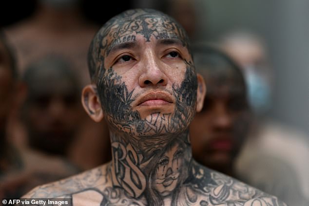 A tattoo-covered prisoner looks on in a cell at the CECOT