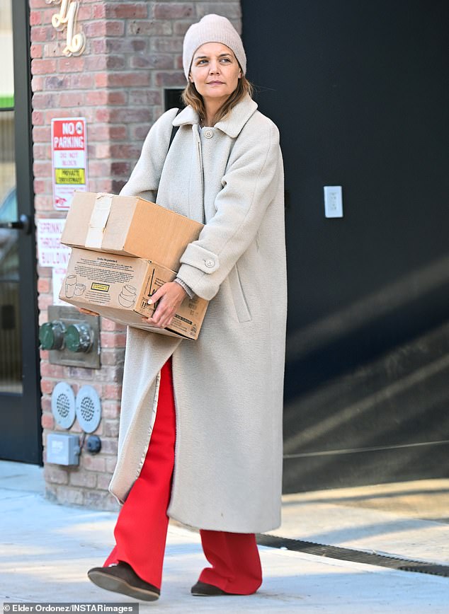Meanwhile Katie looked stylish in a long pale beige coat with a matching beanie cap and red slacks as she carried two boxes