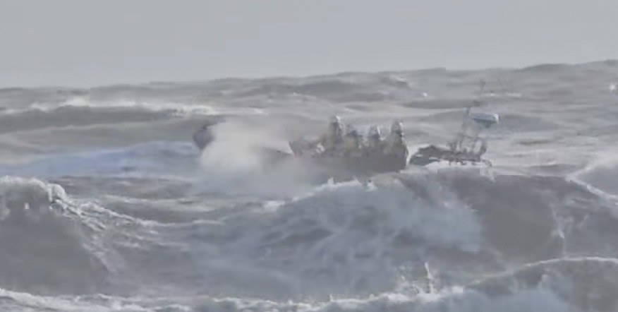 Emergency responders in a small boat amidst large, crashing waves.