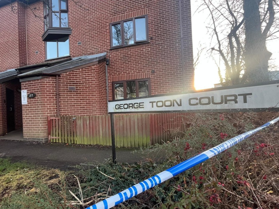 A street sign for "George Toon Court" with blue and white police tape across the foreground, next to a brick building.