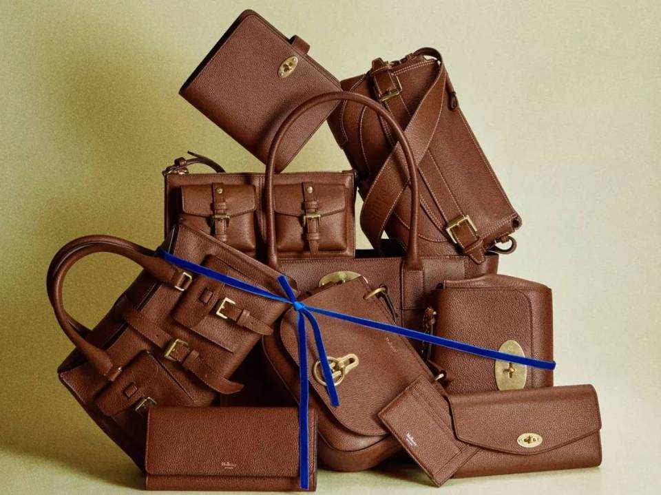 A pile of various brown Mulberry handbags, wallets, and clutches, with a blue ribbon tied around some items.