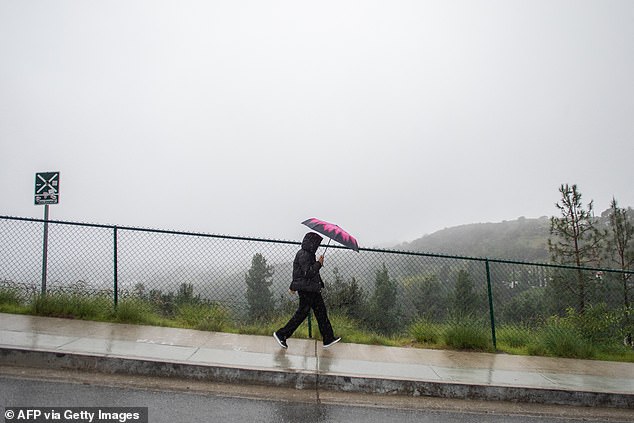 A tourist walks on the rain near the Hollywood sign that has the view blocked by clouds and heavy rain in Los Angeles
