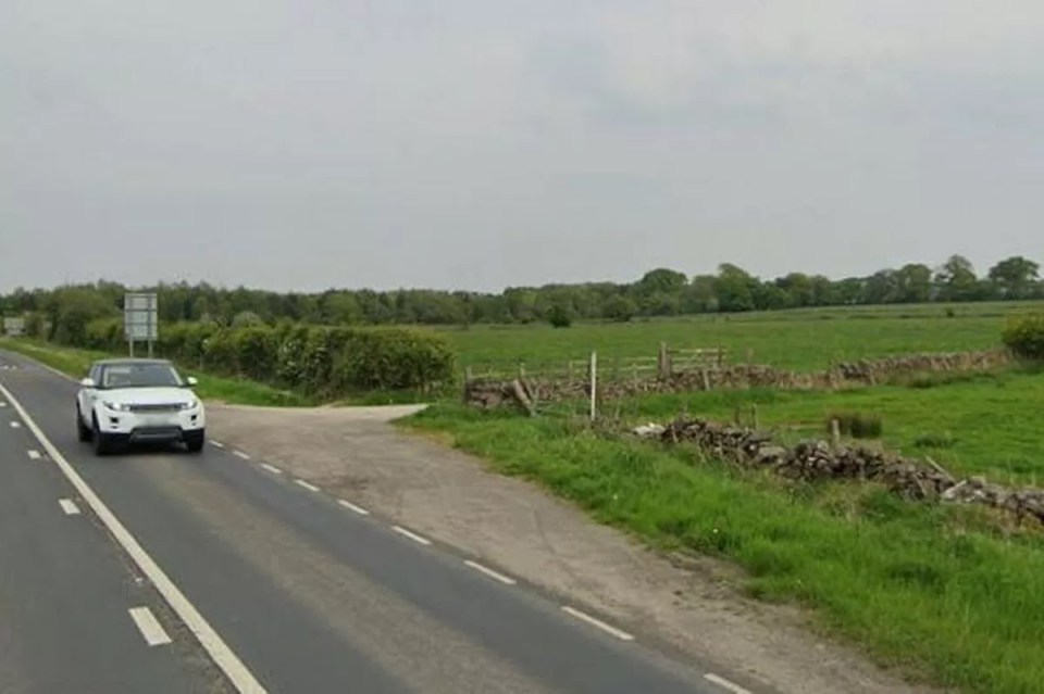 A white Range Rover driving on a highway, with a grassy field and stone wall alongside the road.