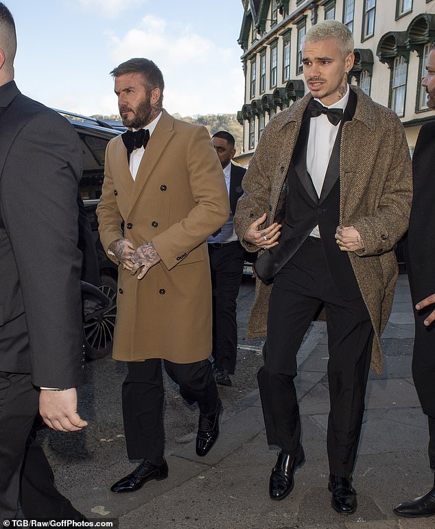 Sir David looked dapper in a brown double-breasted coat layered over a black-and-white tuxedo as he arrived alongside son Romeo, 23