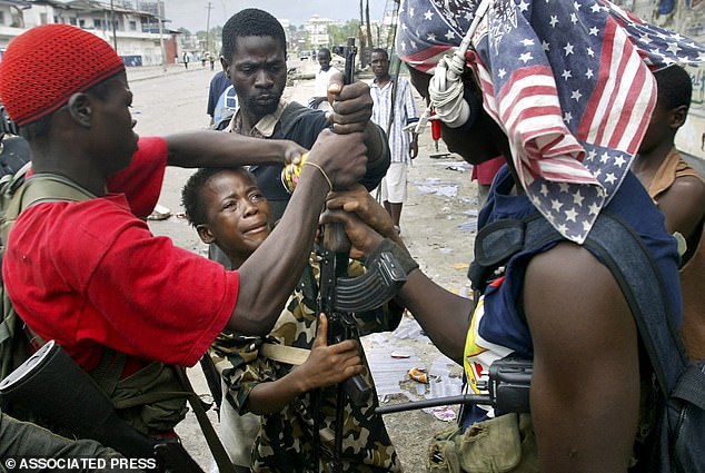 Older rebel fighters wrestle a gun out of the grips of a young fighter who was caught looting with it in Monrovia in 2003