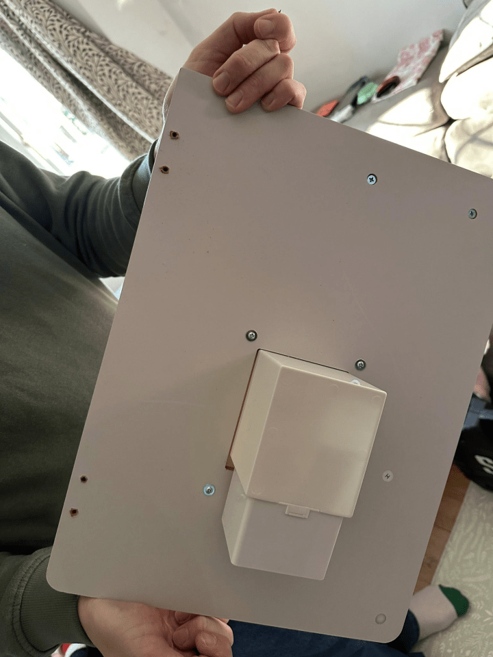 A person holding the back of a toy fridge with screws visible and two holes where a part has fallen off.