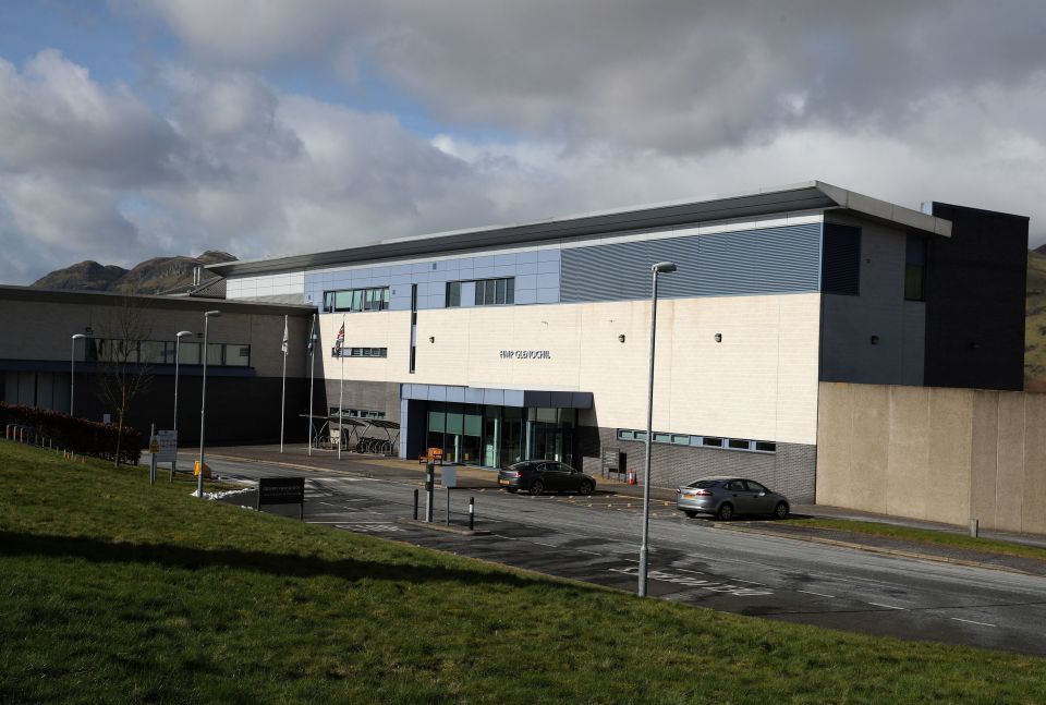 HMP Glenochil prison building, a modern grey and blue building, with a road and grassy area in the foreground.