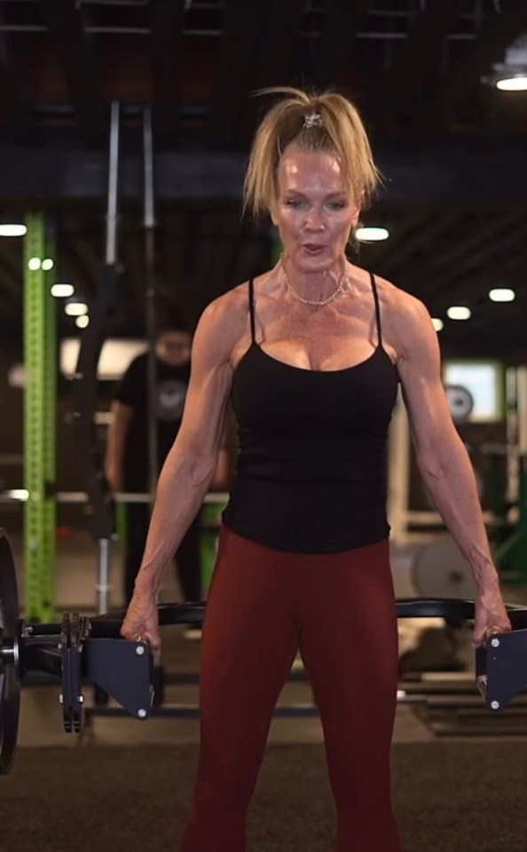 A woman in a black tank top and red leggings lifting weights at a gym.