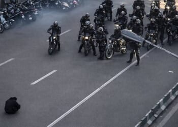 A photo of a lone demonstrator defiantly sitting on the road in front of armed security forces in Iran has gone viral on social media