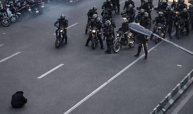 A photo of a lone demonstrator defiantly sitting on the road in front of armed security forces in Iran has gone viral on social media